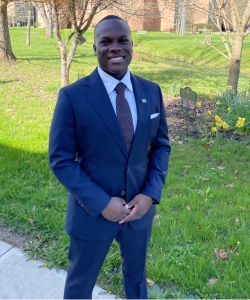 A man in a suit standing outdoors on a college campus.