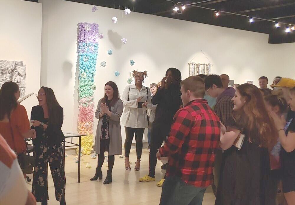 Student in an art gallery receiving an award in a room full of spectators.