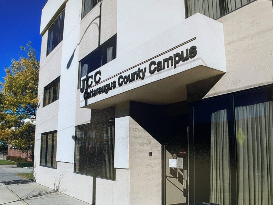 Exterior of Cattaraugus County Campus, a white multistory educational building with bold signage, glass doors, trees, and clear blue skies.