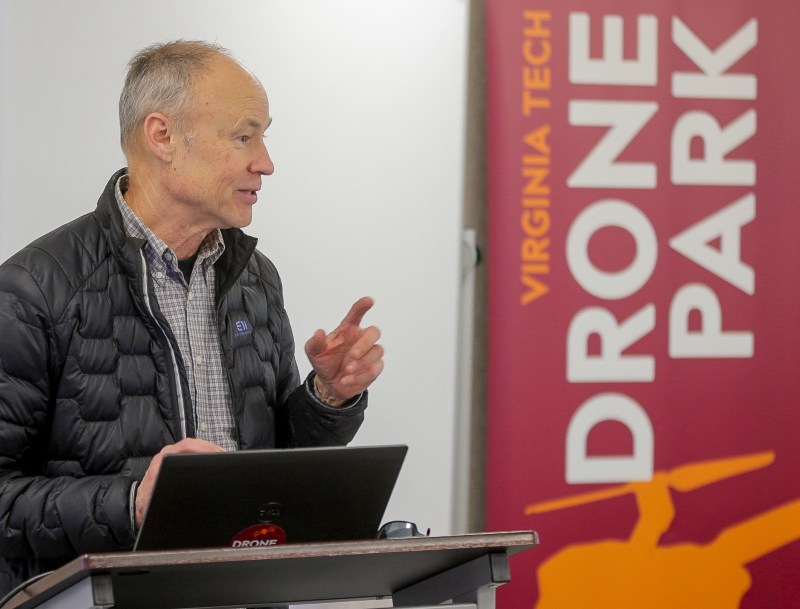 A college instructor talks at a podium with a laptop.