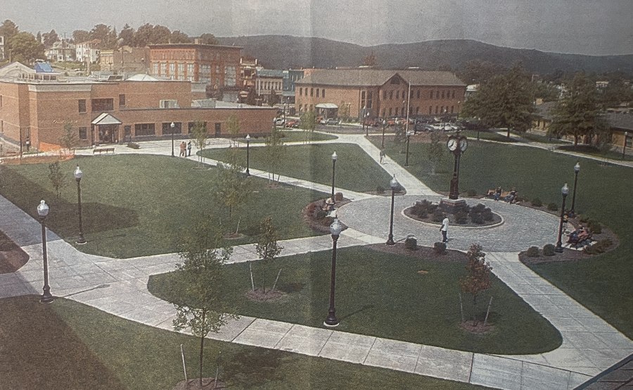 Landscaped campus courtyard, brick buildings, curved paths, lawns, trees, lampposts, and people create a peaceful setting, with mountains beyond.