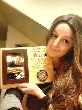 A woman with long hair holding a plaque with stars, a military seal, and picture of a man in front of a flag. 