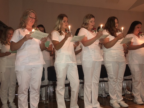 Nurses in white scrubs holding candles and reading the Florence Nightingale Pledge at their pinning ceremony on the SUNY JCC Cattaraugus County Campus.