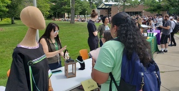 Students visit tables lining the sidewalk at SUNY JCC, while artist in residence Kaycee Colburn talks to a student about the corn husk doll she is holding.