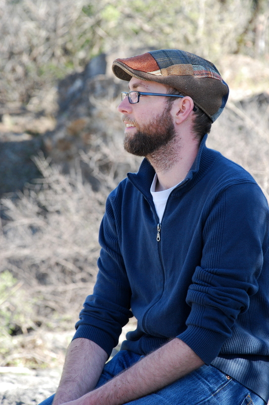 Dr. Colin Kremer is sitting in profile outdoors in a woodland setting.