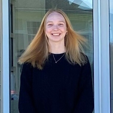 An image of a young woman with long hair standing outside.