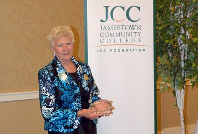 Donna Beal holding glass award in front of SUNY JCC backdrop.