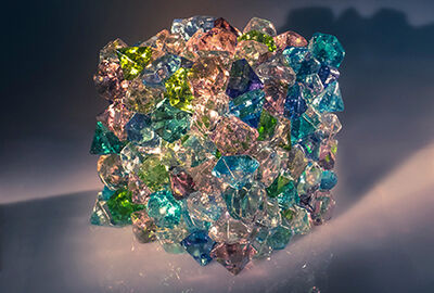 A cube of many different types of glass stands sparkling in a spotlight.