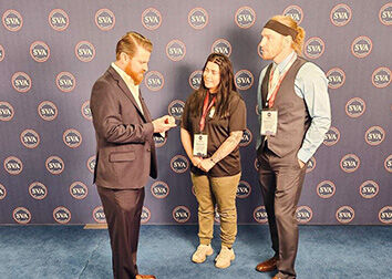 Three people stand talking in front of a backdrop that repeats a circular logo with the letters "SVA."