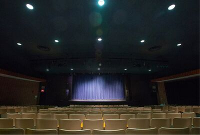 A view from the audience looking at a stage with purple curtains with seats nearby.