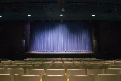 A darkened theater is lit by stage lights with empty seats in the foreground.