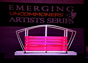 A spotlight shines on a set piece that looks like a bridge on a stage with a sign behind it that says "Emerging Uncommoners Artists Series."