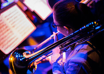 A view over the shoulder of a person playing a horn and reading sheet music.