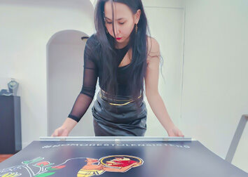 A woman leans over a large piece of graphic art she has created.