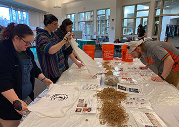 Students stand at a table with three gallon buckets and t-shirts.