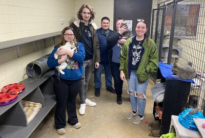 People pose for a photo in an animal shelter with two holding cats.