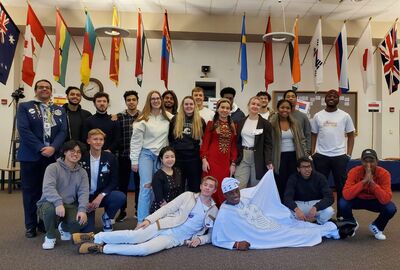 A group of international students pose together in college student union with international country flags hanging in the background.