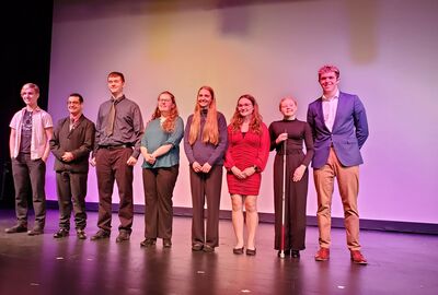 Eight smiling students lined up for a photo on a theater stage.