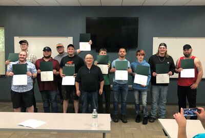 A group of students pose together in a classroom while holding graduation certificates.