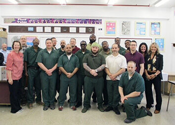A group of people stand together in a room during a graduation celebration for SUNY Jamestown Community College's Prison Education Program.