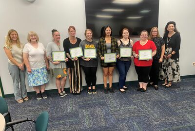 Six students hold certificates of completion while joined by three college faculty members.