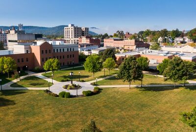 Overhead view of a college campus with buildings, large lawn, and clock tower with a city scape in the background.