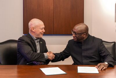 Two men shake hands while sitting at a conference table.