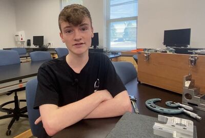 A student sitting at a lab desk with mechanical technology equipment and tools laying on the desk nearby.