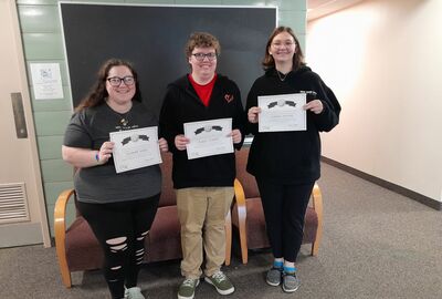 Three students hold certificates together for a photo.