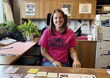 A smiling woman sits at a desk in a school counselor's office.
