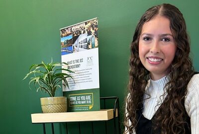 Alexis Lundmark smiles with a green wall background plant and small information banner about the SUNY JCC Foundation behind her.