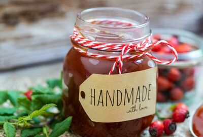 A wax candle in glass jar with a tag that reads handmade with love.