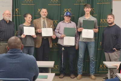A group of machining/cnc advanced manufacturing hold up certificates of completion in front of a SUNY JCC logo backdrop.
