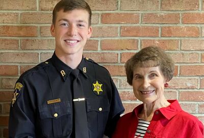 A person wearing a police uniform stands by a woman as they hold a scholarship check together.