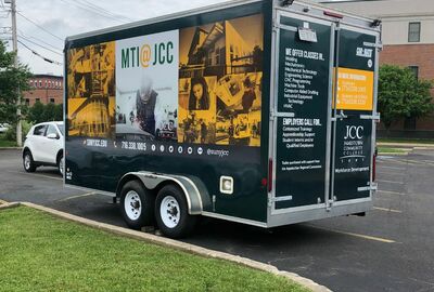 A trailer in a parking lot. The trailer has on it images and information about JCC's MTI programs and class offerings.