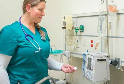A nursing student in scrubs checks a medical machine.