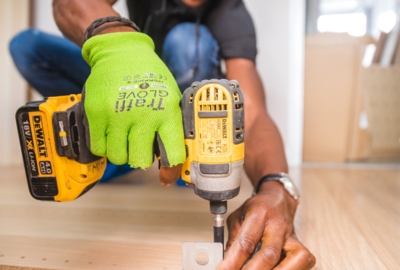 A person user a power drill to attach a metal piece to wood.
