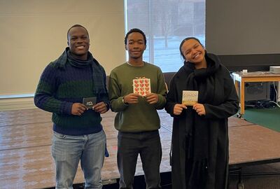Three people holding gift cards pose in a college student union.