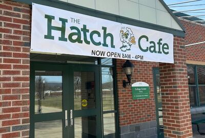 A banner at a building entrance that reads The Hatch Cafe open 8 a.m. to 4 p.m. with a Jayhawk mascot logo.