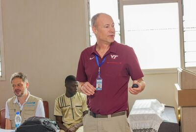 A college instructor talks in class while two students behind him listen.