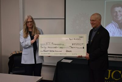 Two people hold a large check showing a $40,000 donation to the JCC Foundation for the Daniel F. Courtine Endowment.
