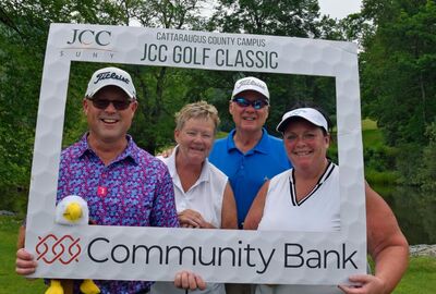 Four people wearing golf attire pose for a photo behind a large white frame that reads JCC Golf Classic with the SUNY JCC logo.