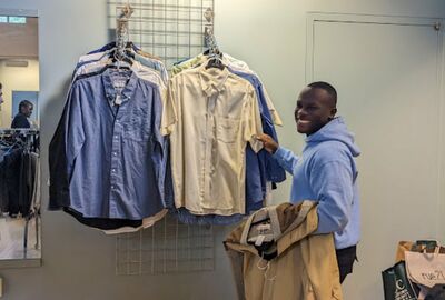 A person smiles while hanging up dress shirts in a college career closet.