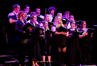 A large college choral group singing on stage.