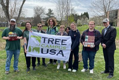 A group of students and campus leaders pose outside with banner that reads Tree Campus USA.