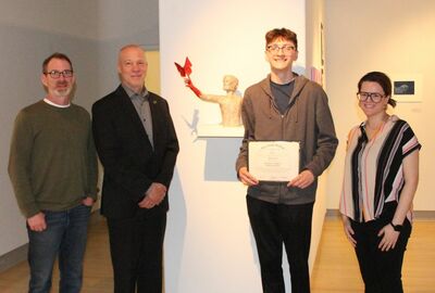 A student holding a certificate of achievement poses with three others in an art gallery.