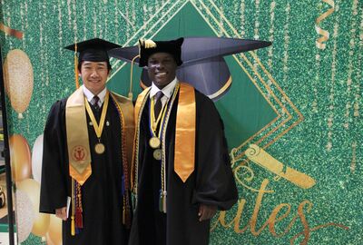 Two people wearing graduation caps and gowns smile.