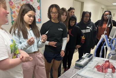 Students visiting the respiratory therapy department of a hospital with one holding and looking at a plastic tube.