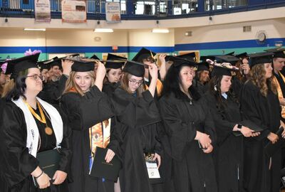 Students dressed in graduation caps and gowns move the tassels on their caps.