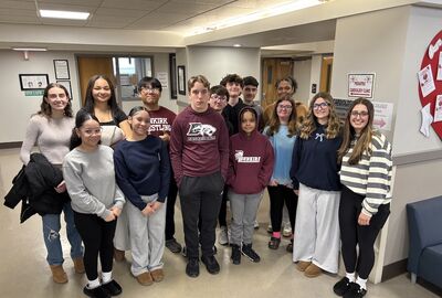 A group of high school students together for a photo in a hospital floor lobby.